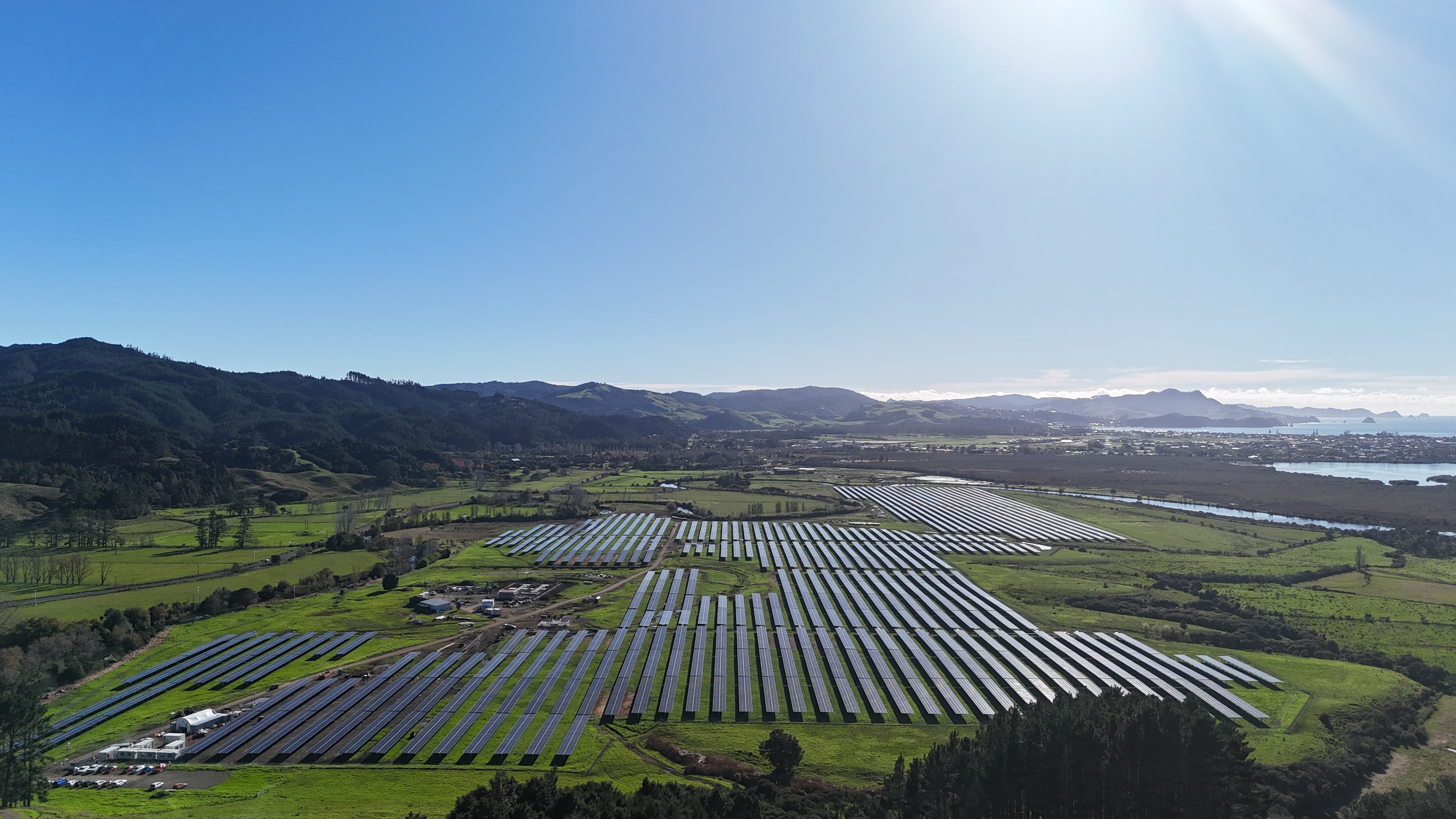 A view of thousands of solar panels on green fields with blue sky and sun in the sky